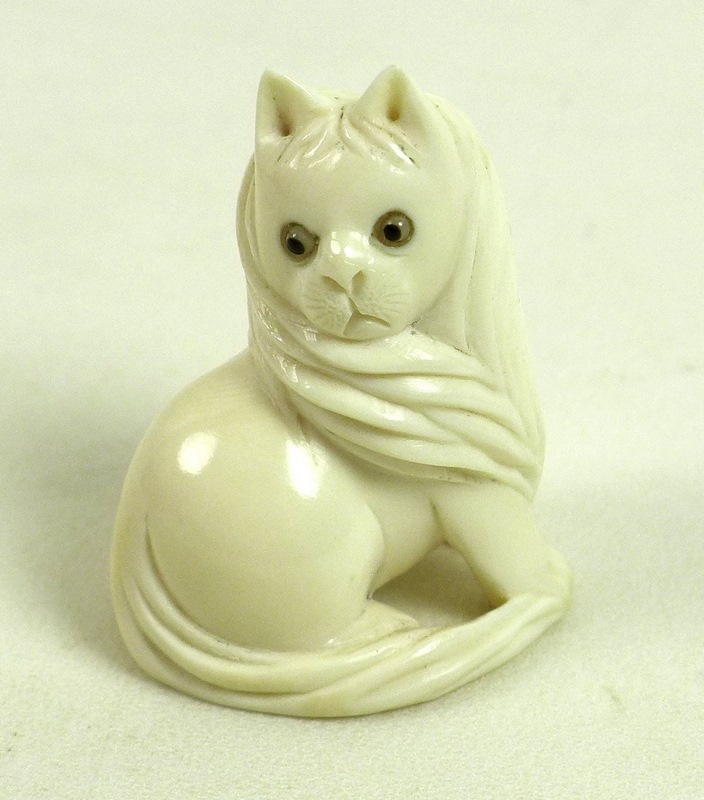 A Japanese ivory netsuke, circa 1900, carved as a cat sitting looking over it's right shoulder,