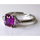 A platinum, ruby and diamond three stone ring, the central cushion cut pink ruby of approximately