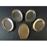A group of five silver oval photograph frames, comprising a set of four frames, each 14cm oval,