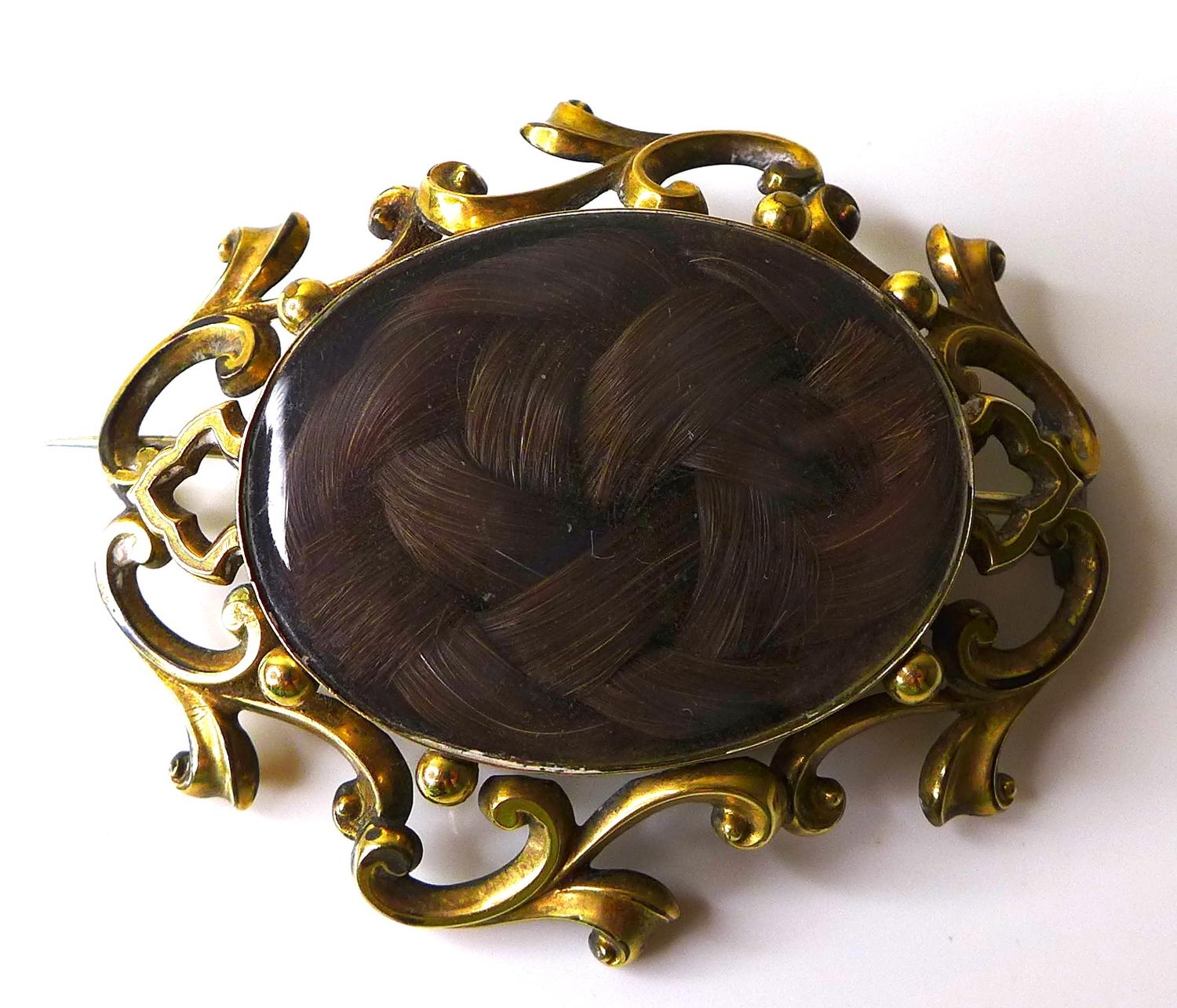 A Victorian yellow metal mourning brooch, with scrolling frame around a glazed oval window set