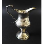 A George III silver cream jug, decorated in Rococo style with a repousse cottage and farm scene