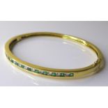 A 14ct gold, emerald and diamond bangle, set with alternating brilliant cut emeralds and diamonds,