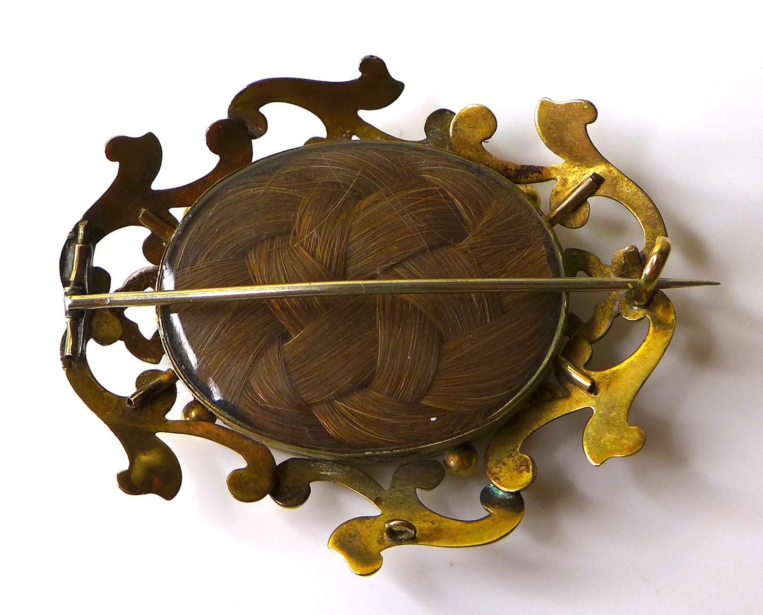 A Victorian yellow metal mourning brooch, with scrolling frame around a glazed oval window set - Image 2 of 2