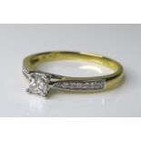 An 18ct gold and diamond ring with princess cut central stone, flanked by shoulders set with