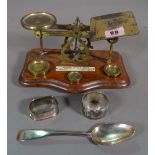 A set of brass postage scales, a silver tea spoon and two napkin rings, (qty).