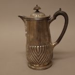 A silver hot water jug, with a partly fluted body and hinged lid,
