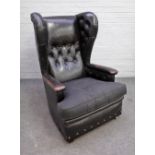 A mid-20th century black leather upholstered wingback armchair on squat block supports,