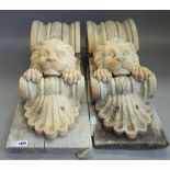 A pair of composite stone corbels, each with lion head mask mounted on a pine plinth,