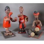 A group of three hardwood carved tribal figures depicting tribesman in red in various poses.