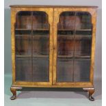 A mid-20th century figured walnut display cabinet with arch panel doors on pad feet,