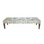 A large rectangular footstool with grey and blue foliate upholstery on tapering square supports,