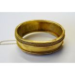 A Victorian gold oval hinged bangle, the front with applied decoration in the classical taste,