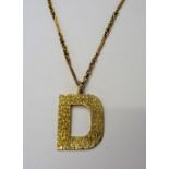 A gold pendant, designed as the initial D, having a bark textured finish,
