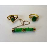 A gold ring, claw set with an oval jade between circular cut diamond set two stone shoulders,