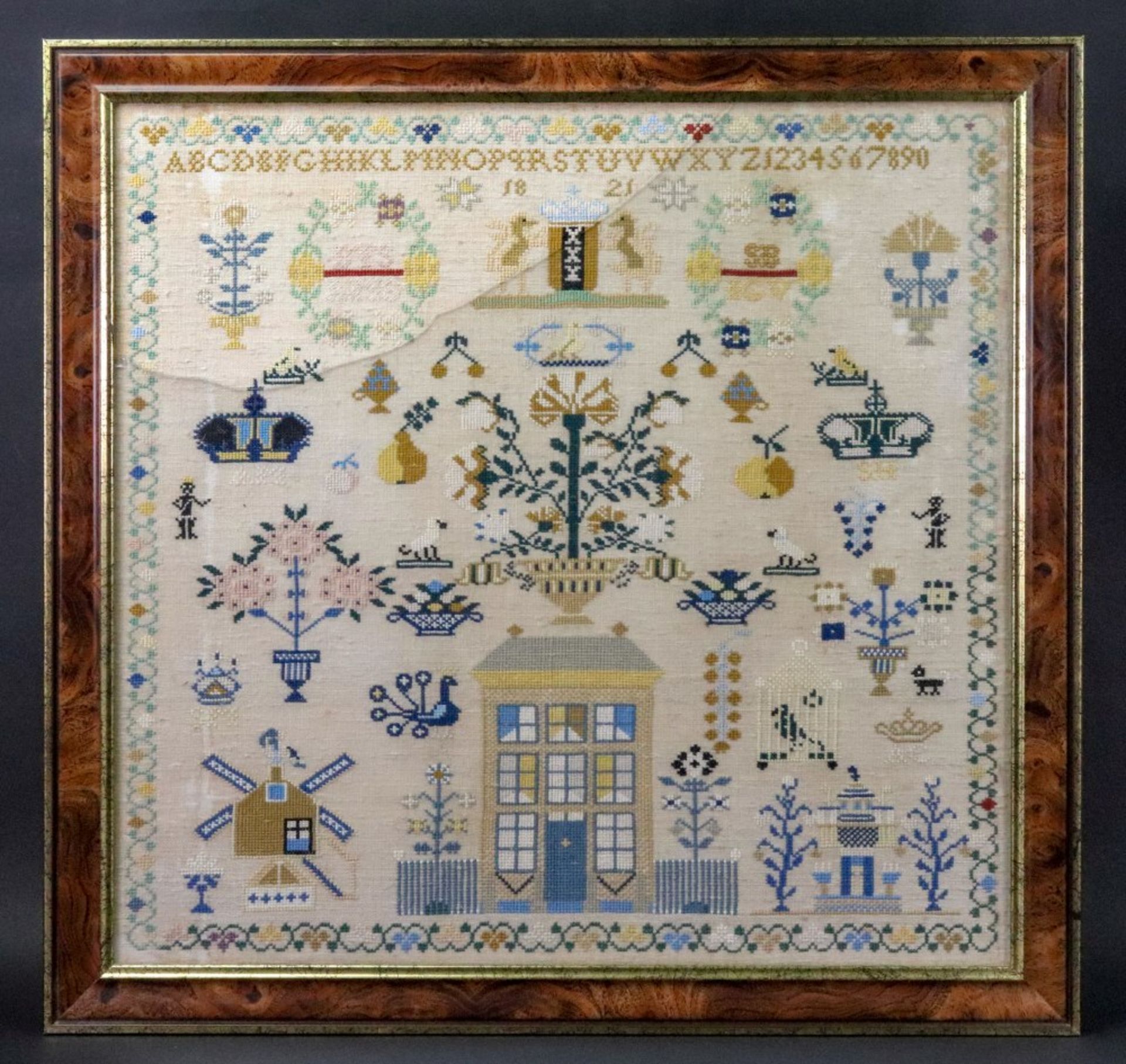 A needlework sampler, dated 1821, with a central house flanked by a windmill and another building,