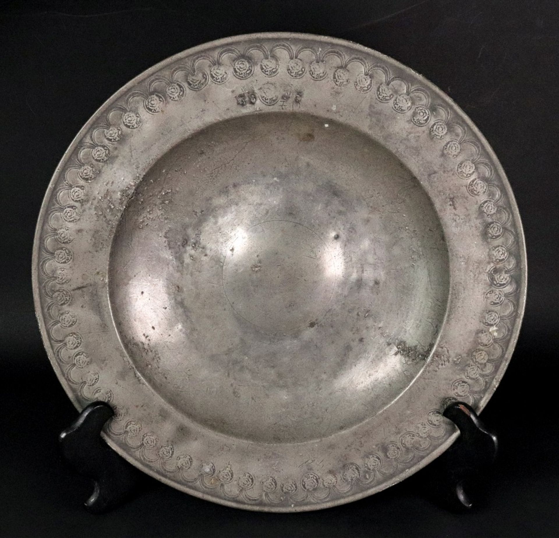 A broad rimmed pewter charger, 17th century, with punched arcading linked by repeated makers mark T.