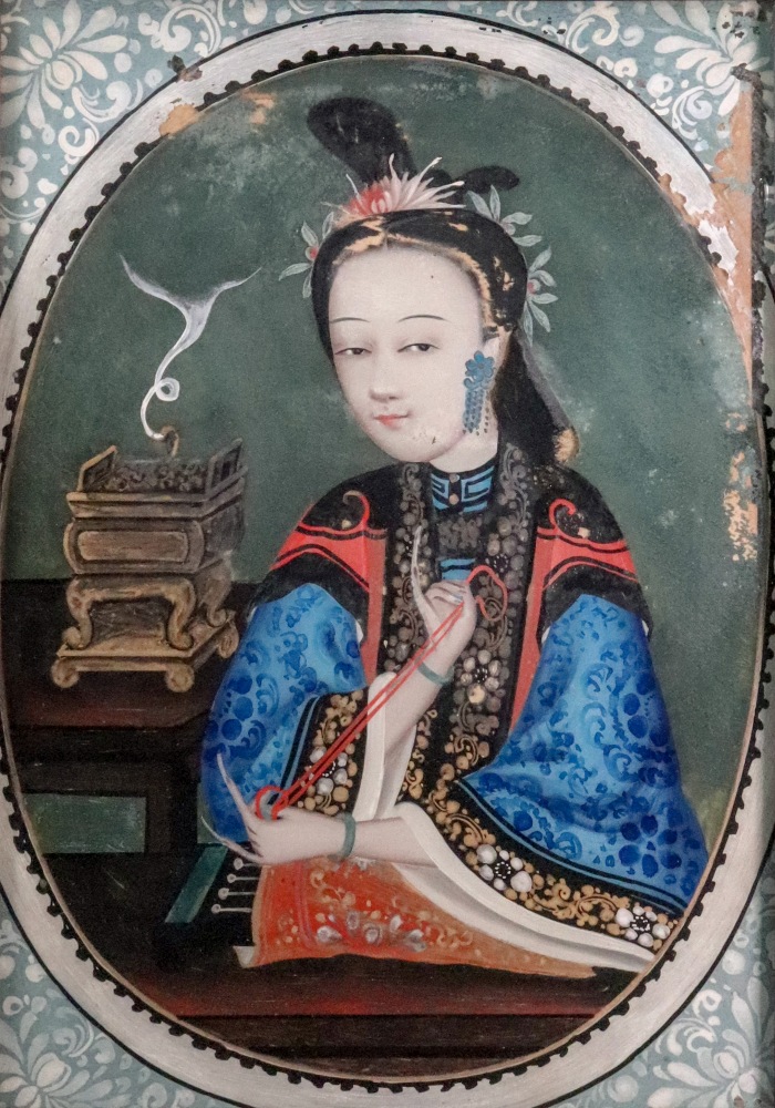 A Chinese portrait of a woman, 18th/19th Century, sewing at a table, a censer to her left hand side,