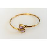 A 9ct gold and amethyst bangle, collet set with two oval cut amethysts, in a twistover design,