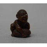 A Japanese wood netsuke of a blind beggar, 19th century, attempting to lift his distended scrotum,