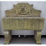 A reconstituted stone wall fountain with lion mask spout over rectangular reservior on scroll