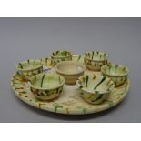 A Chinese circular pottery tray and six cups, Tang dynasty, each piece splashed in green and ochre,
