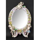 A Dresden porcelain framed oval mirror, late 19th century, applied with three putti and flowers,