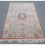 A Qum silk rug, the ivory field with a madder roundel, pale indigo spandrels,