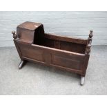 An 18th century oak rocking cradle, with integral hood and turned finials, 91cm wide x 60cm high.