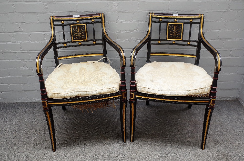 A pair of Regency style parcel gilt ebonised open armchairs on sabre supports,