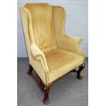 A George II style wingback armchair on square cabriole supports, united by turned stretcher,