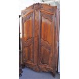 An 18th century fruitwood armoire with carved arched cornice over a pair of shaped panel doors,