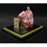 A Japanese doll, 20th century, 21cm high, in glazed ebonised display case.