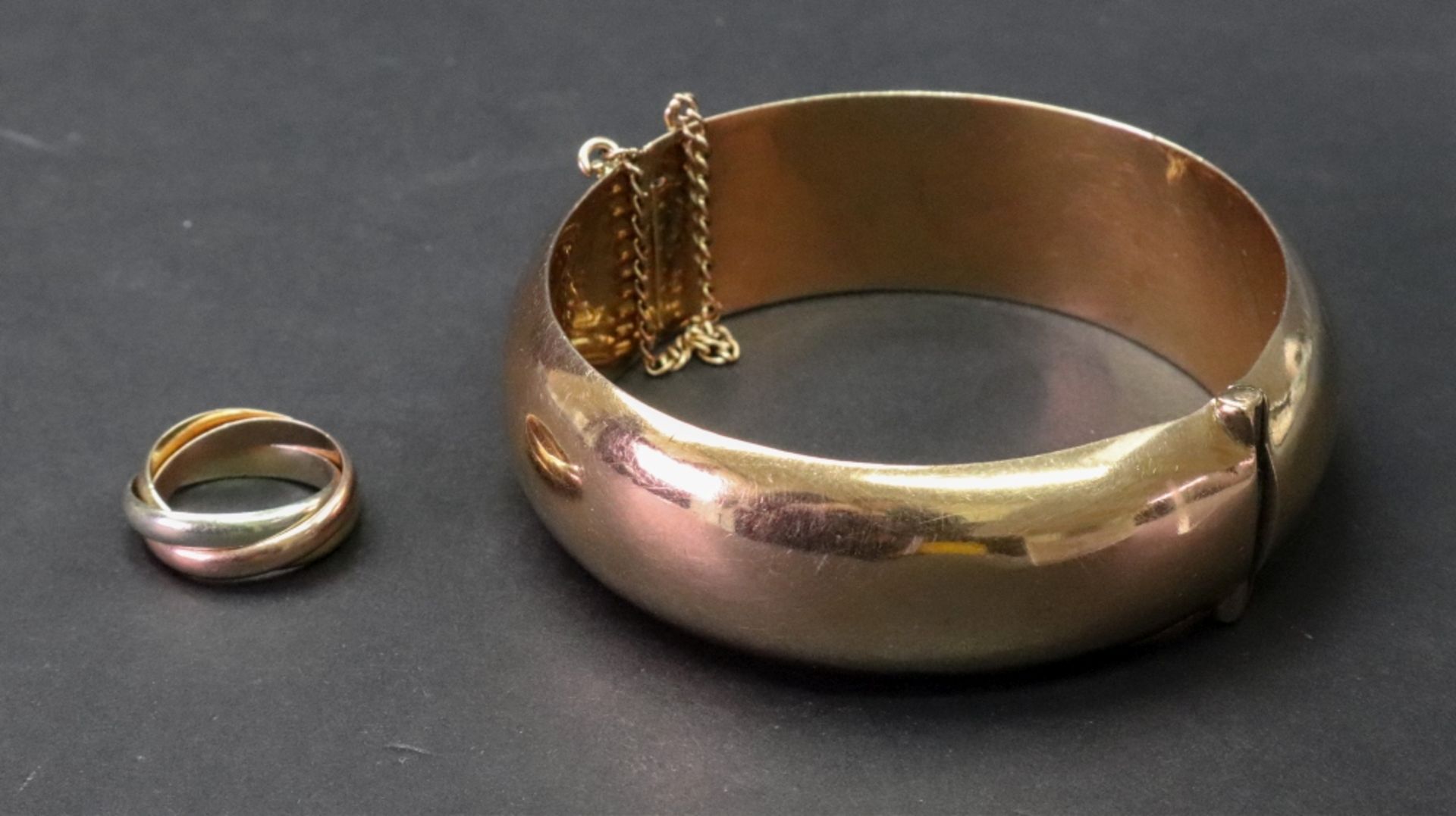 A pink precious metal hollow hinged bangle of oval design, complete with safety chain,