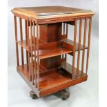 An Edwardian walnut square revolving bookcase, the moulded top above two tiers with slatted sides,