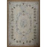 A needlework rug in Aubusson style, centred by flowers in a floral wreath, on a light grey ground,