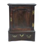 A George III oak table top cupboard, the shaped raised and fielded panel door enclosing two shelves,