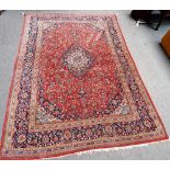 A Kashan carpet, Persian, the madder field with a bold indigo and ivory medallion,