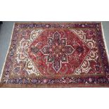 An Heriz carpet, Persian, the madder field with a bold indigo medallion, ivory spandrels,