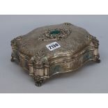 A shaped rectangular hinge lidded trinket box, the hinged lid with a cabochon green gem set centre,