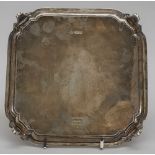 A silver salver, of shaped square form, raised on four tapered curved legs,