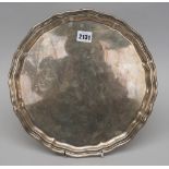 A silver salver, of shaped circular form, having a pie-crust rim, raised on three scrolling feet,