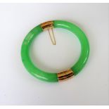 A circular treated jade hinged bangle, on a snap clasp, fitted with a safety chain.