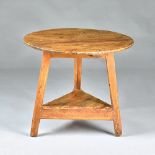 An early 19th century pine cricket table, on three splayed supports united by platform undertier,