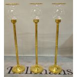 A set of three 20th century brass and glass standing hurricane lamps, 119cm high.