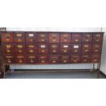 A stained pine apothecary cabinet with three rows of nine drawers, on metal stand,