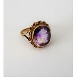 A gold ring, collet set with a cushion shaped amethyst within a ribbon twist surround,