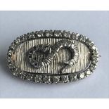 A white precious metal and diamond set brooch, of oval design, the central diamond set S motif,