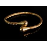 A yellow precious metal torc bangle of rope-twist design and in tapered terminals, detailed '21k',