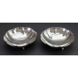 A pair of circular dishes, detailed sterling silver, with lobed and fluted sides, on three feet,