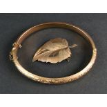 A 9ct rose gold hinged bangle, engraved with scrolling foliage,